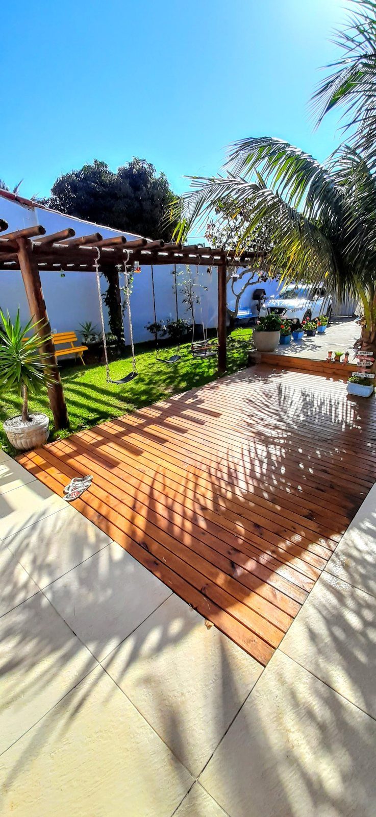 Deck de madeira ao sol, com pergolado e balanço no jardim