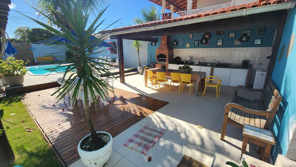 Varanda gourmet com mesa e cadeiras amarelas, deck de madeira e a piscina ao fundo
